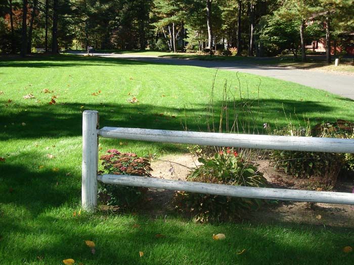 A white wooden fence surrounds a lush green lawn