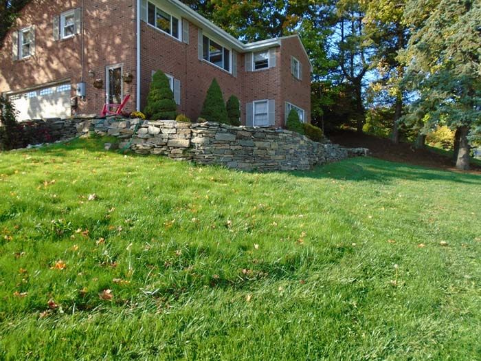A large brick house sits on top of a lush green hillside surrounded by trees.