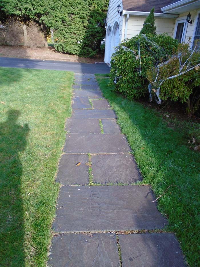 A stone walkway leading to a house with a lot of grass.