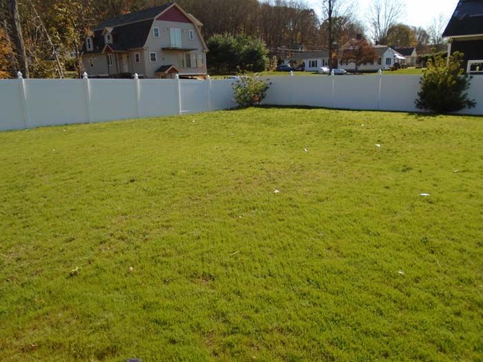A large lawn with a white fence and a house in the background
