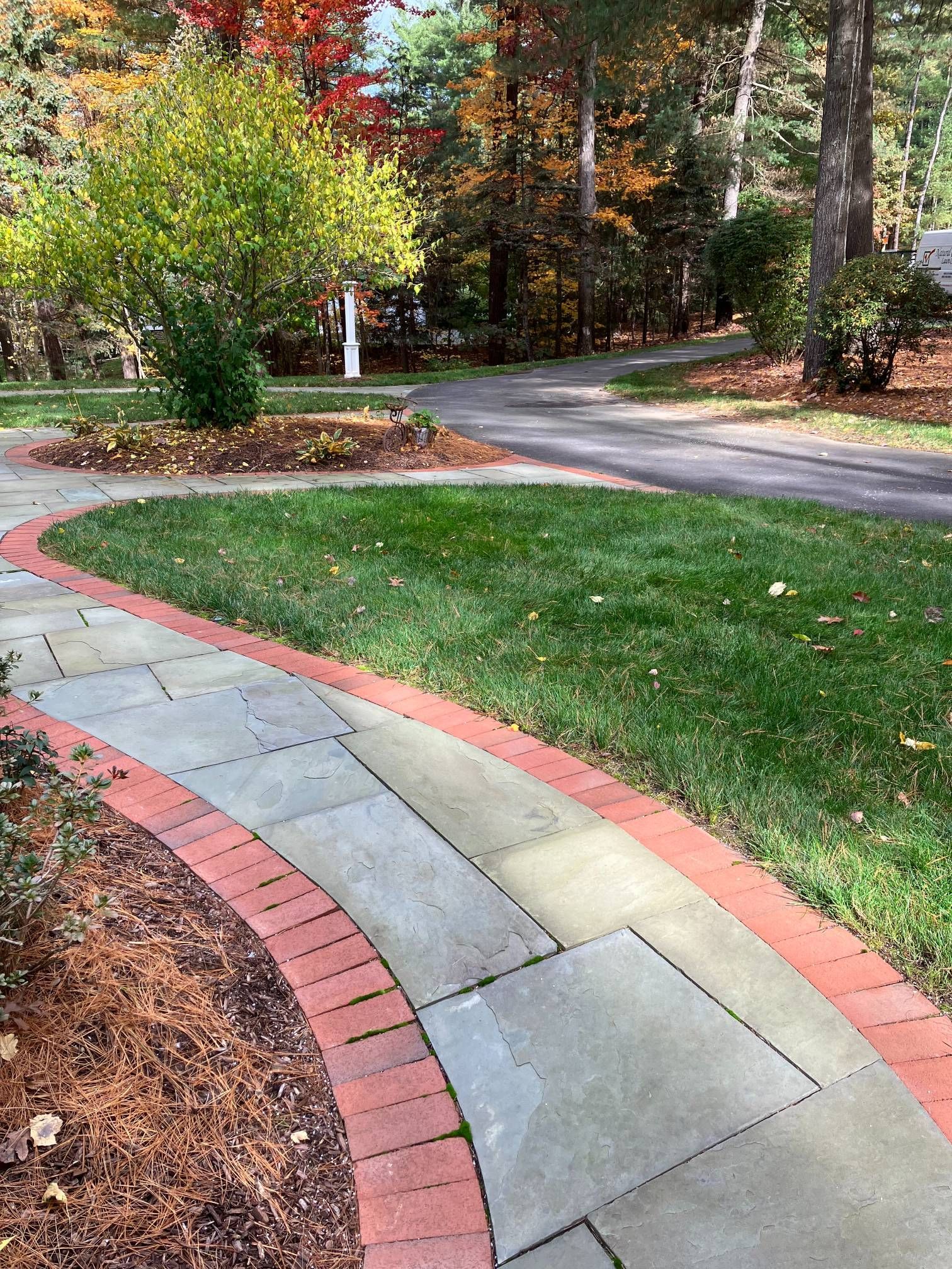 A stone walkway with a brick border is surrounded by grass and trees.