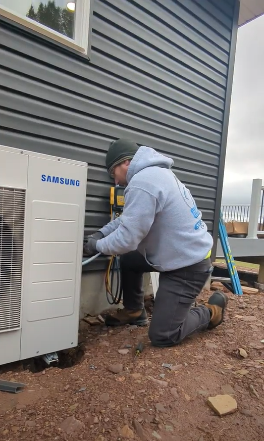 A man is working on a samsung air conditioner outside of a house.