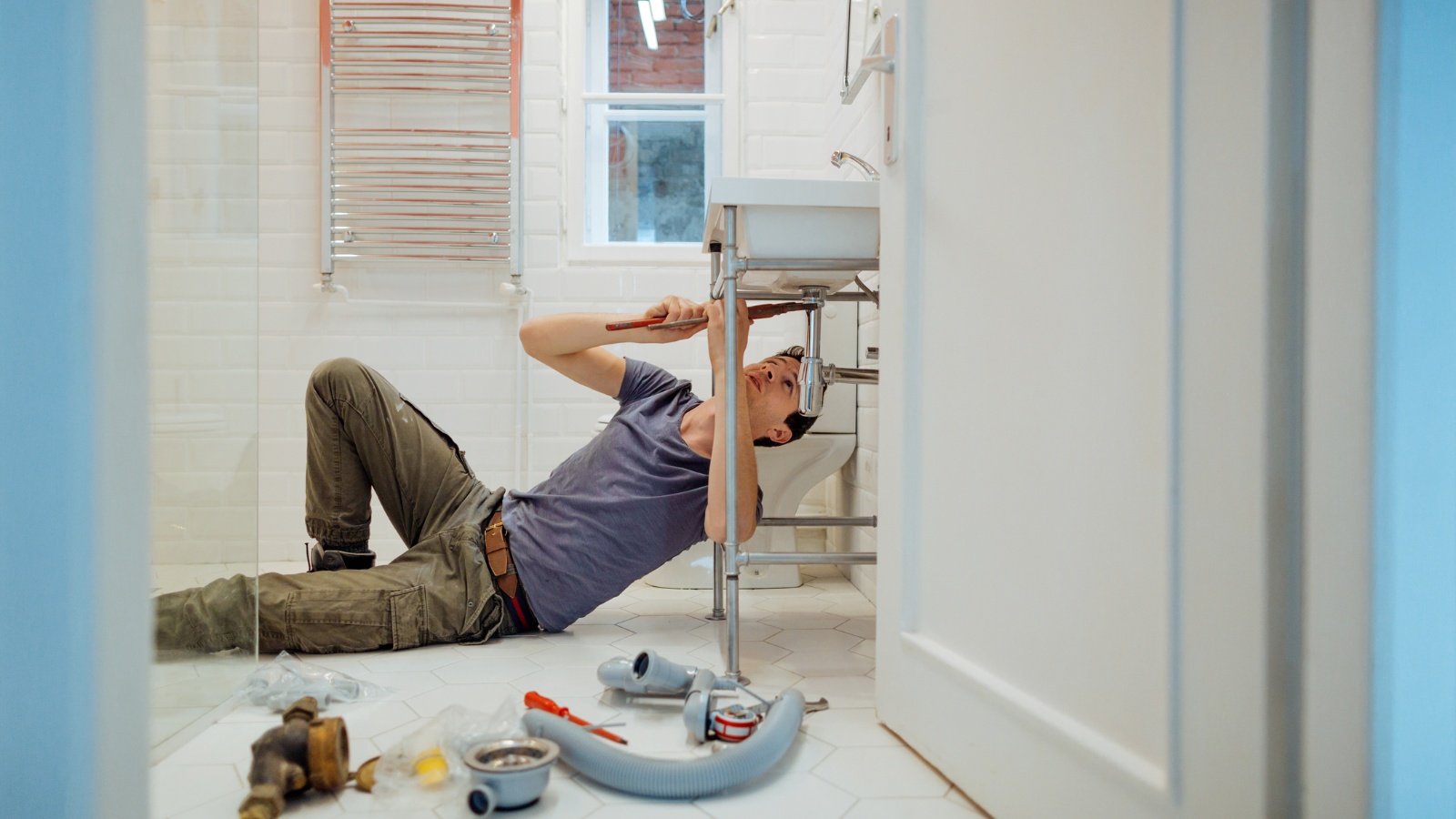 A plumber is laying on the floor fixing a sink in a bathroom WS Mechanical Blog
