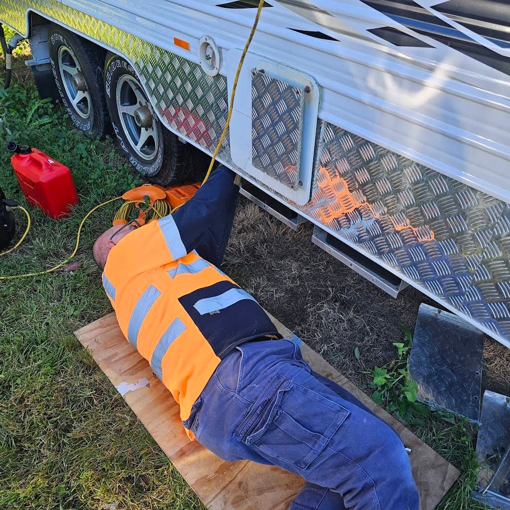 Man in Safety Vest Works Under a Trailer, Lying on Plywood — Glenn Rowe Auto Electrics In Helensvale, QLD