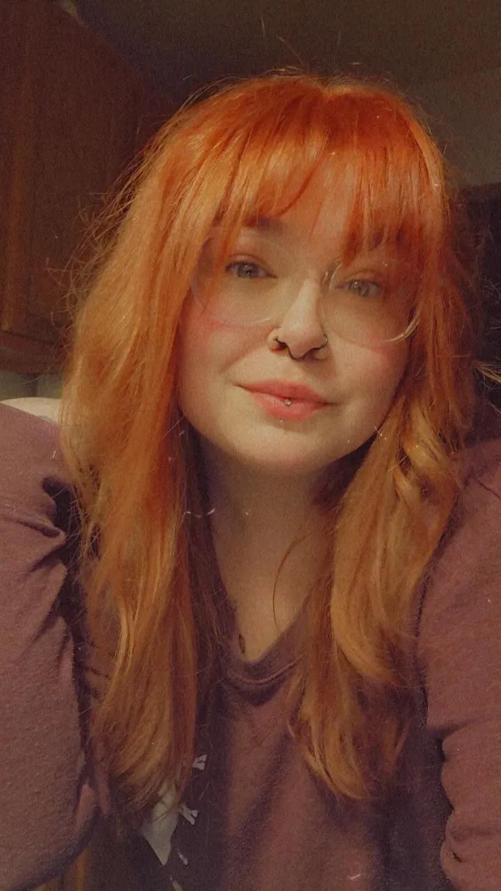 A woman with red hair and glasses is smiling for the camera.