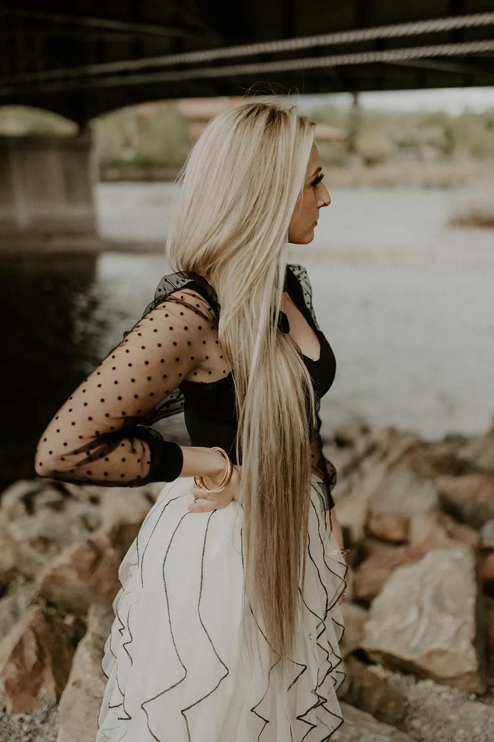 A woman with very long blonde hair is standing under a bridge.