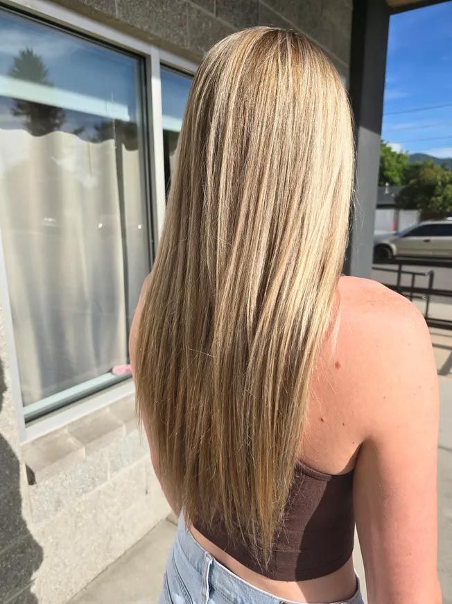 A woman with long blonde hair is standing in front of a window.