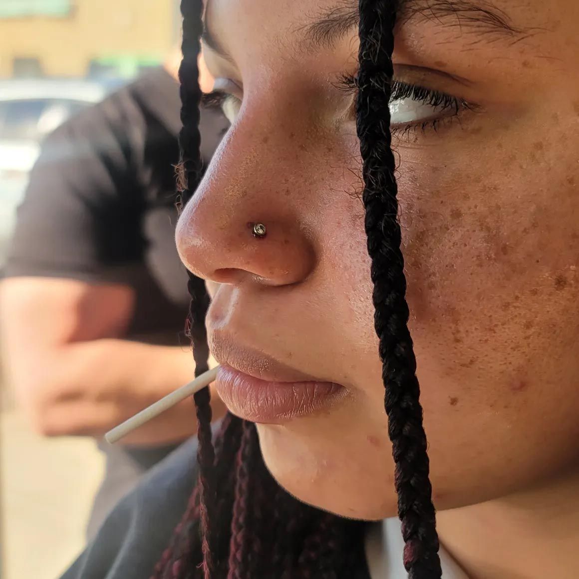 A close up of a woman 's face with braids and a nose ring.