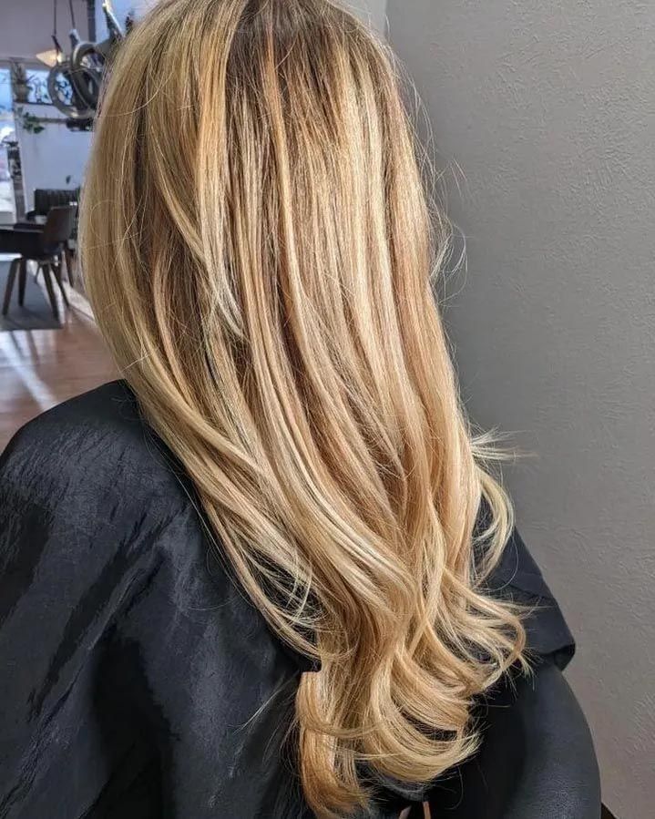A woman with long blonde hair is sitting in a chair in a salon.