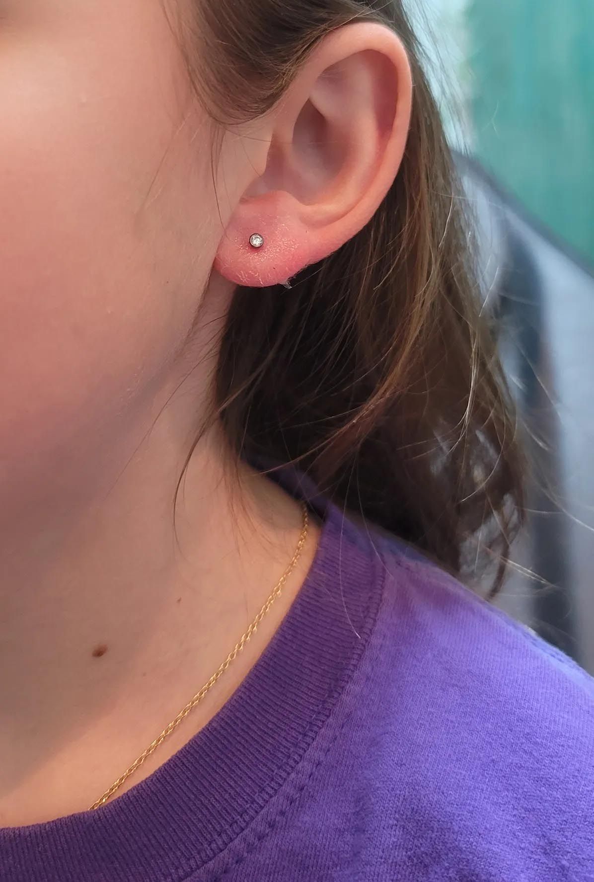 A close up of a person 's ear with earrings and a purple shirt.