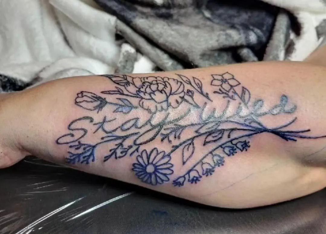A person has a tattoo on their arm that says stay wild