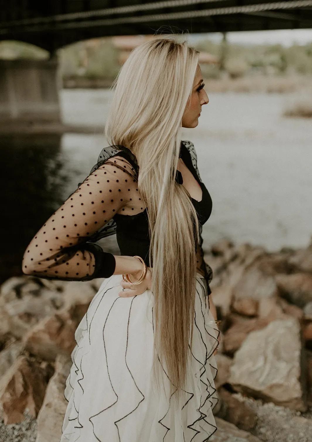 A woman with very long blonde hair is standing next to a body of water.