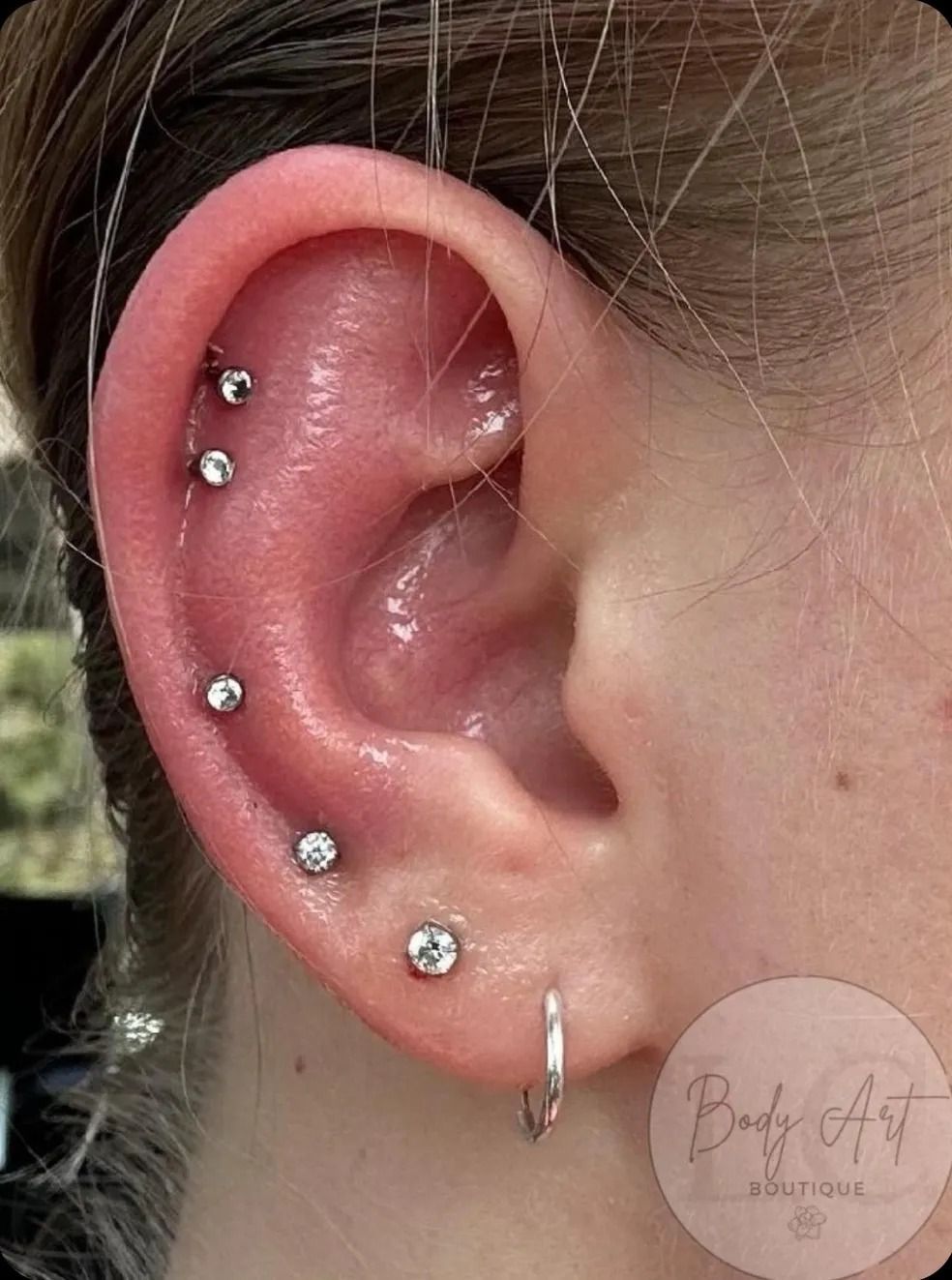 A close up of a woman 's ear with multiple piercings.