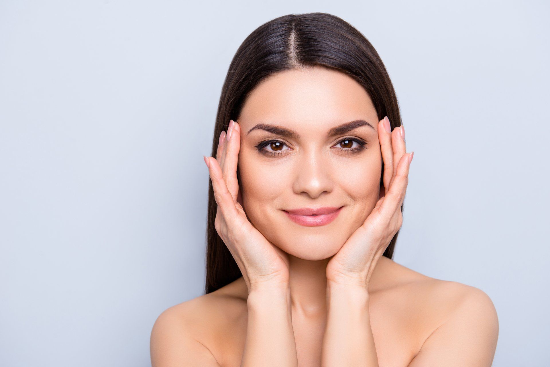 A woman is touching her face with her hands and smiling.