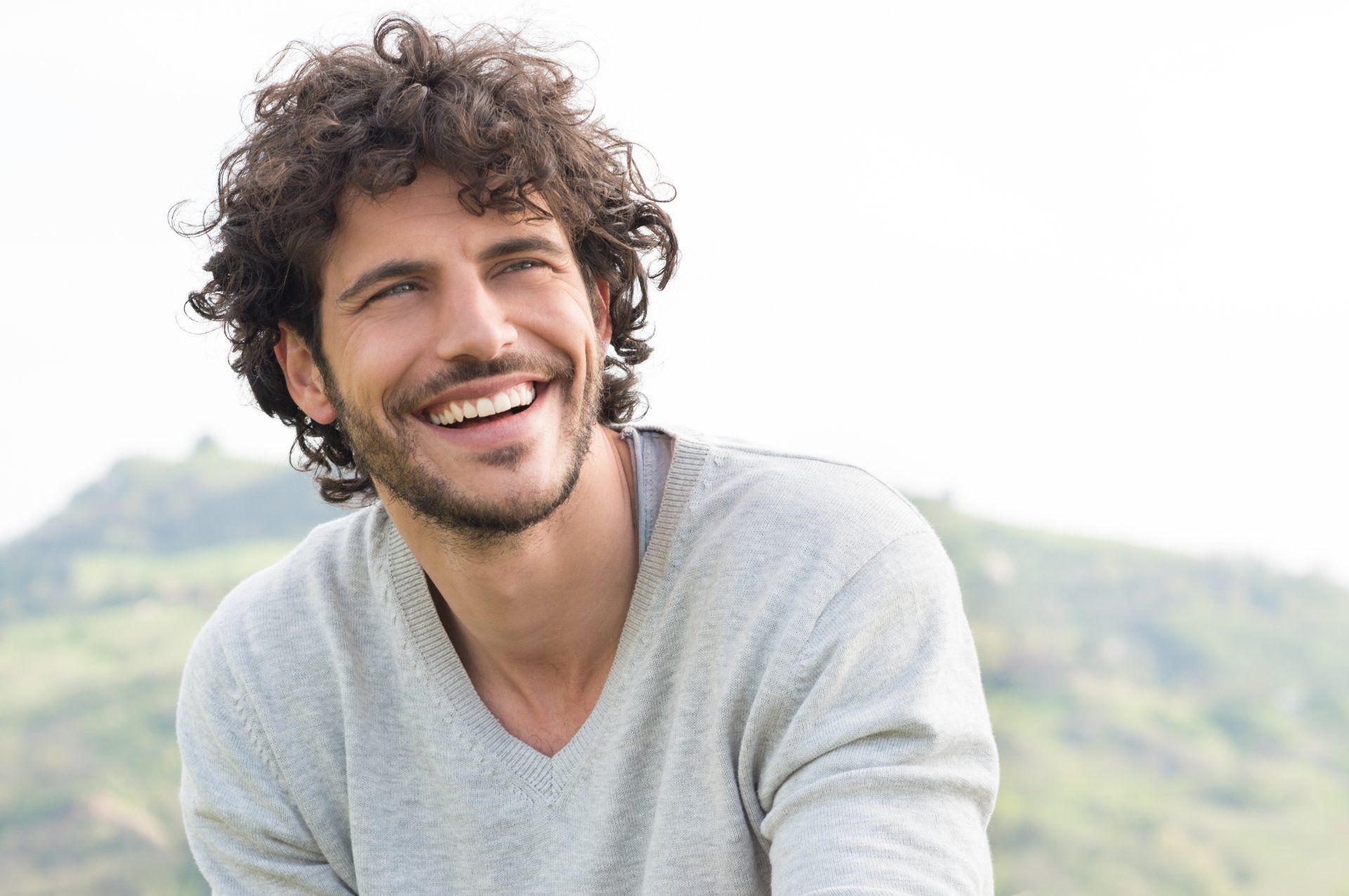 A man with curly hair and a beard is smiling.