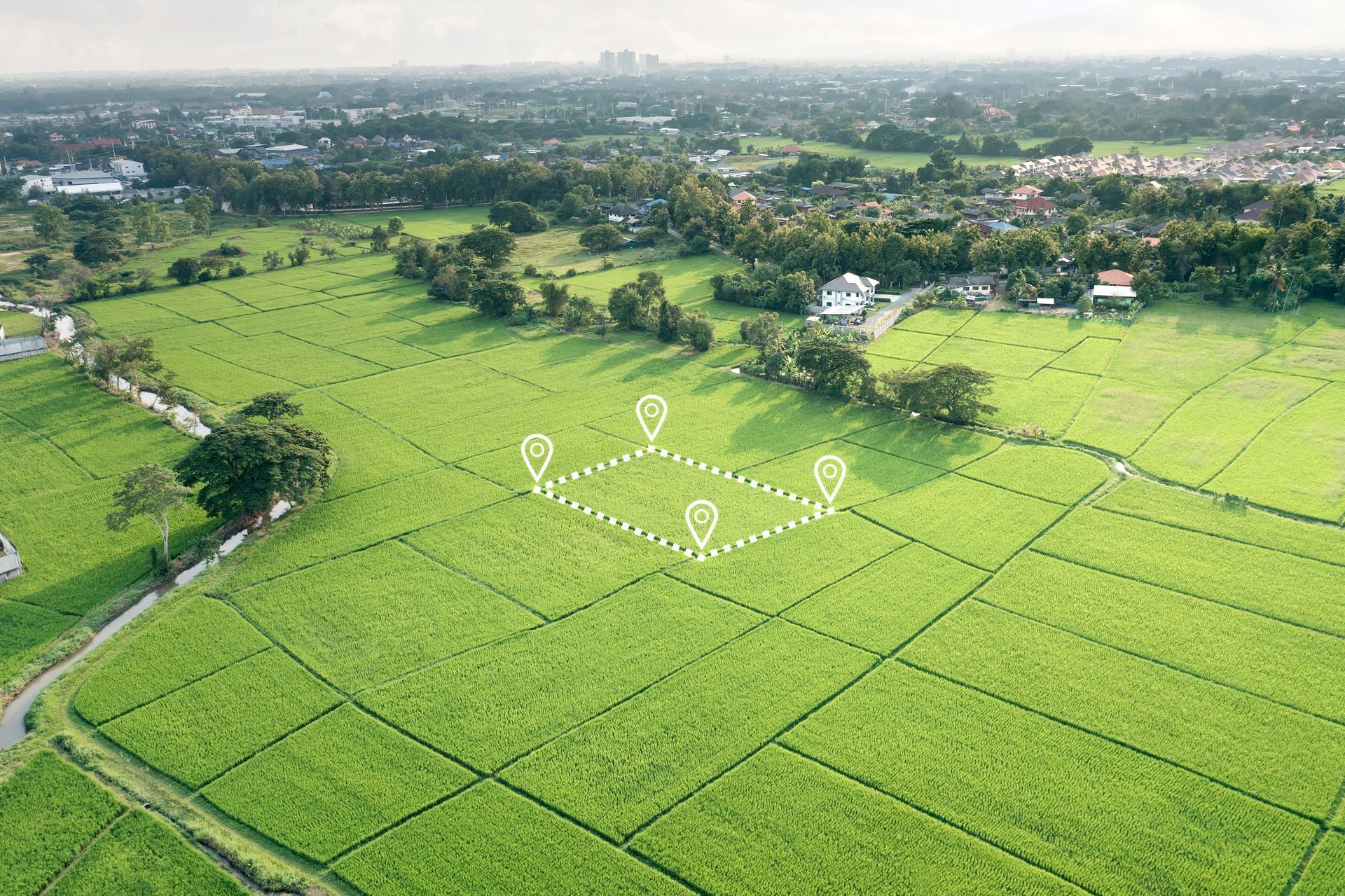 Aerial view of a green field with a marked-off square, set amidst a rural landscape, likely land for sale.