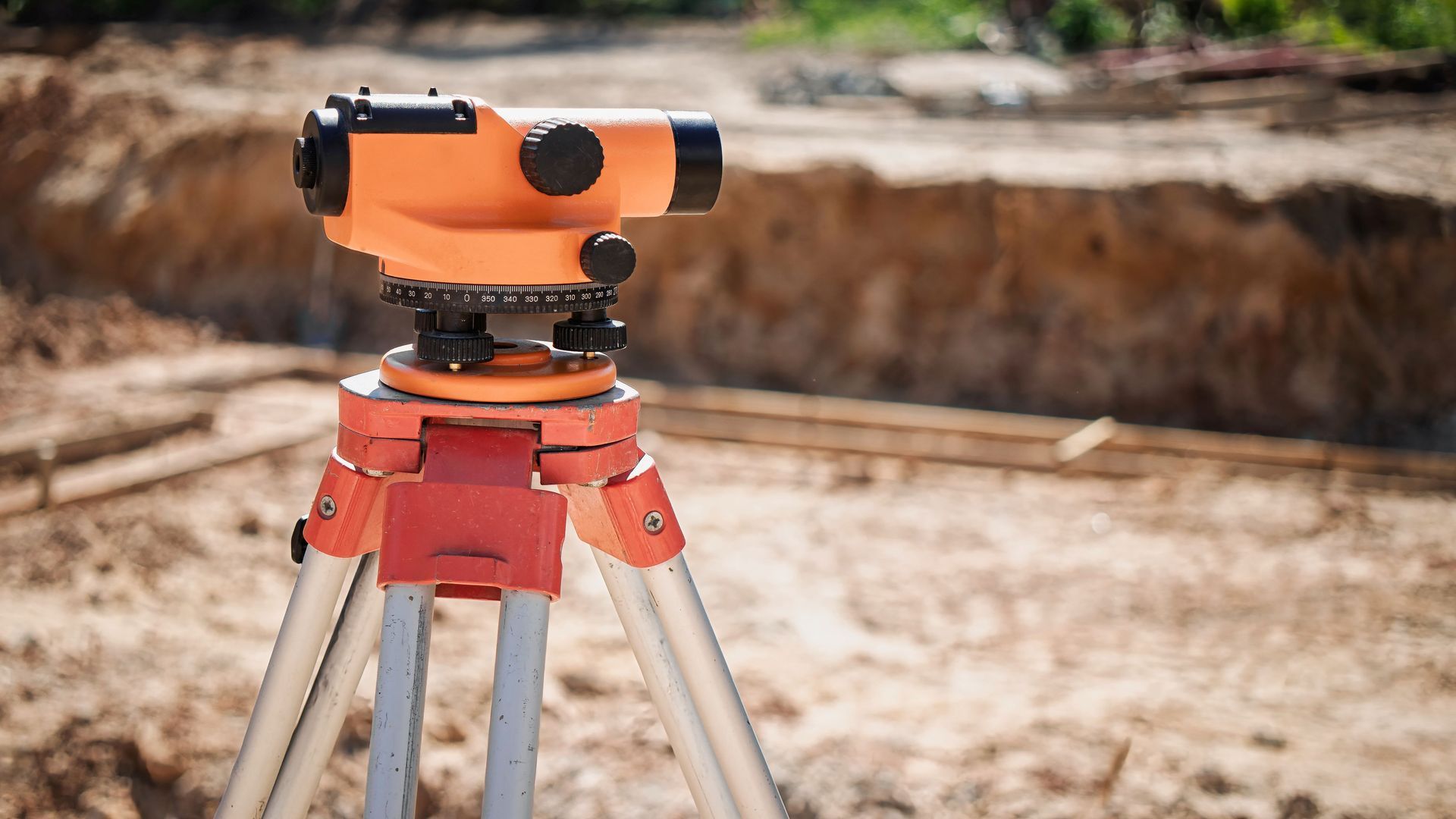 Orange surveying level on tripod, in front of a construction site.