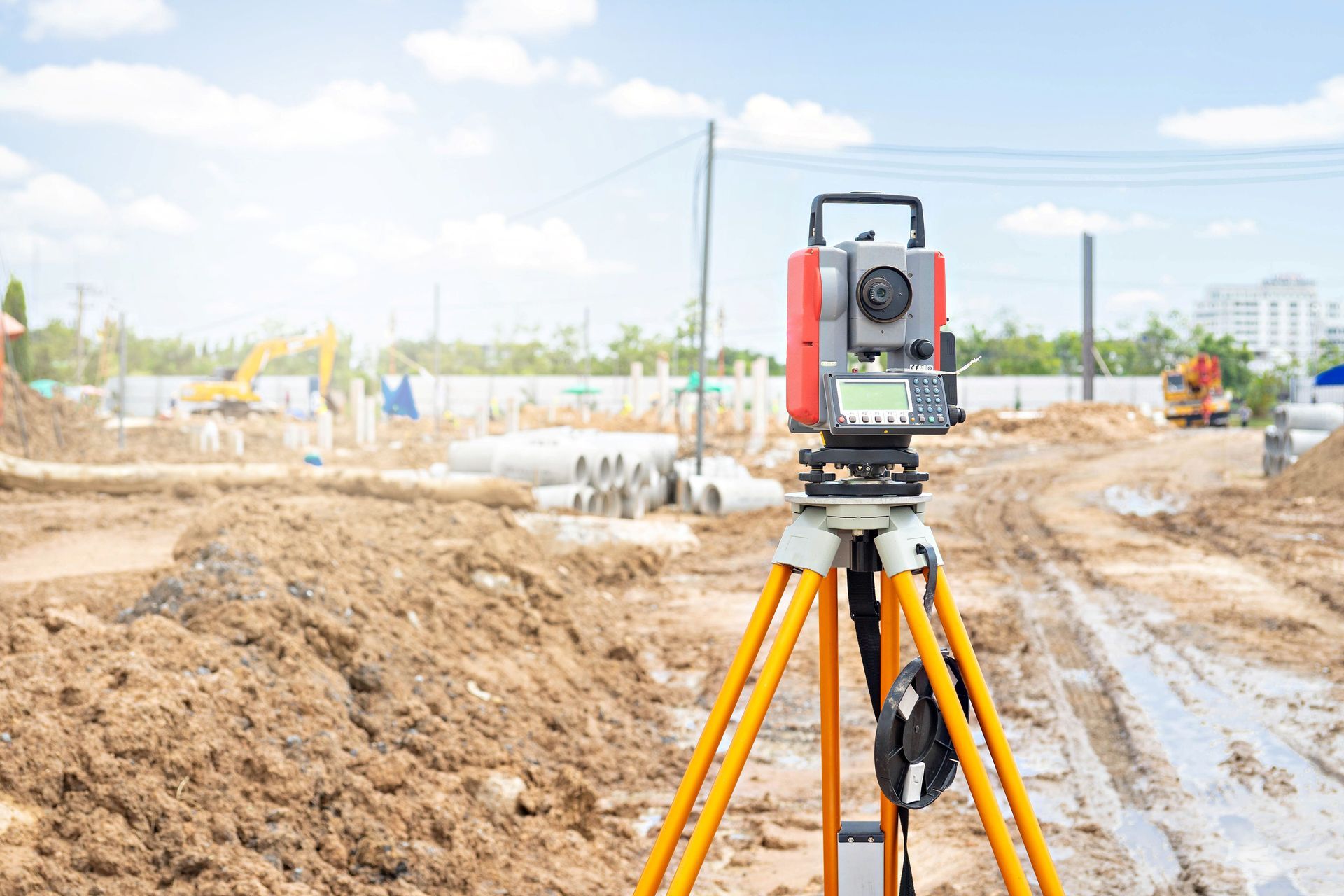 A total station surveying instrument on a tripod, at a construction site.