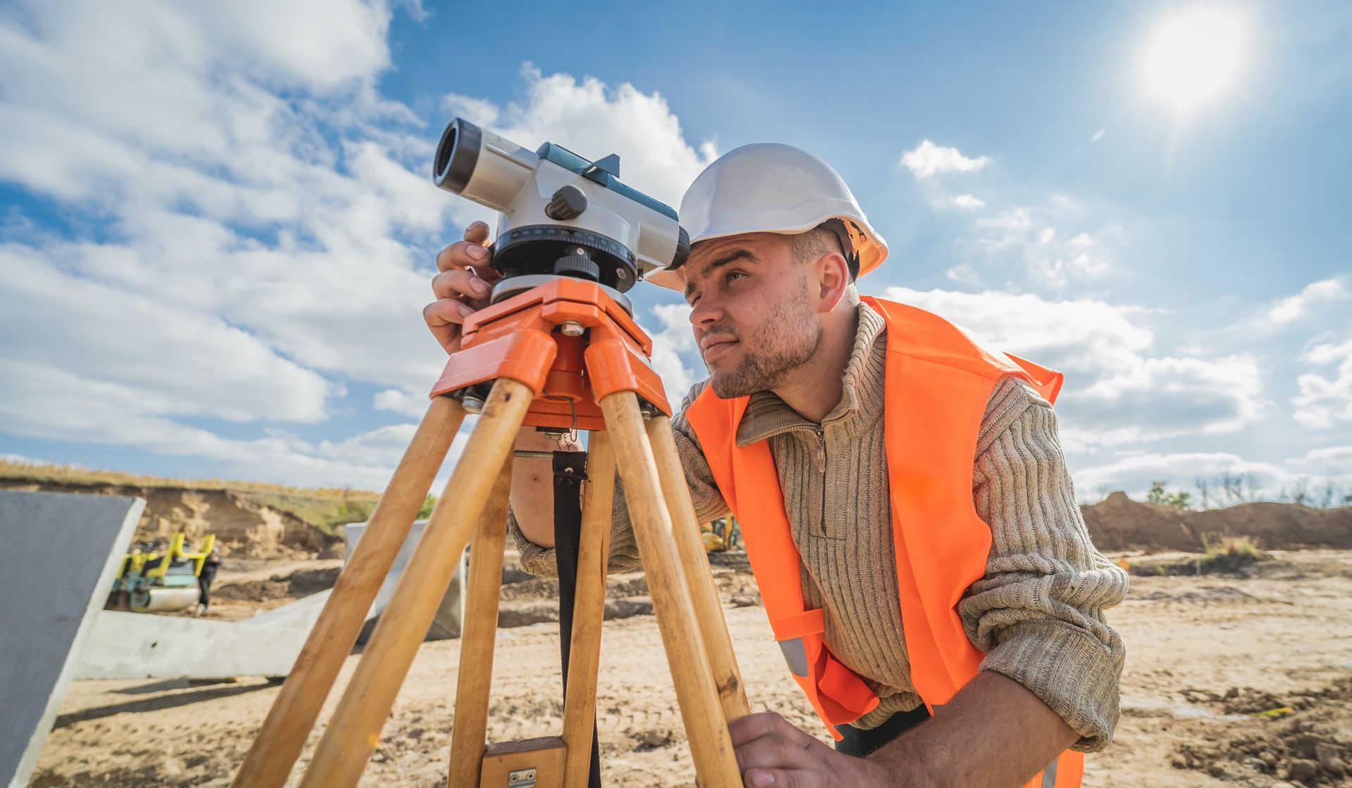 Land surveyor in hard hat and safety vest using a level on a tripod outdoors. Land surveyor in hard hat and safety vest using a level on a tripod outdoors.