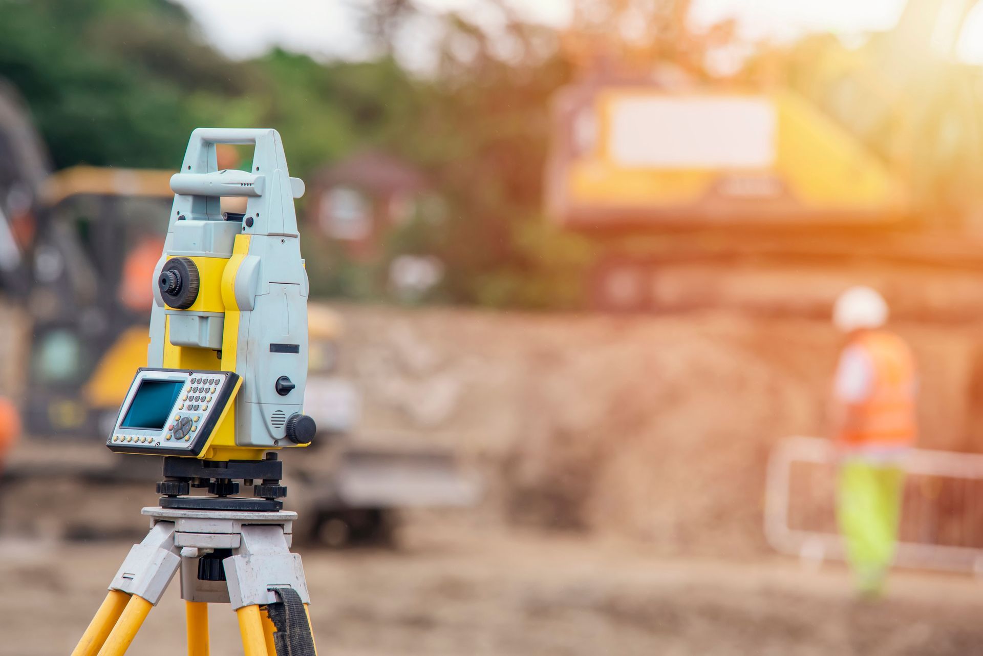 Surveying equipment on a tripod, construction site background. Bright sunlight.