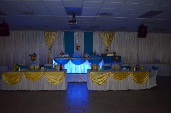 Decorated banquet hall stage with blue lighting and yellow-draped tables at the front