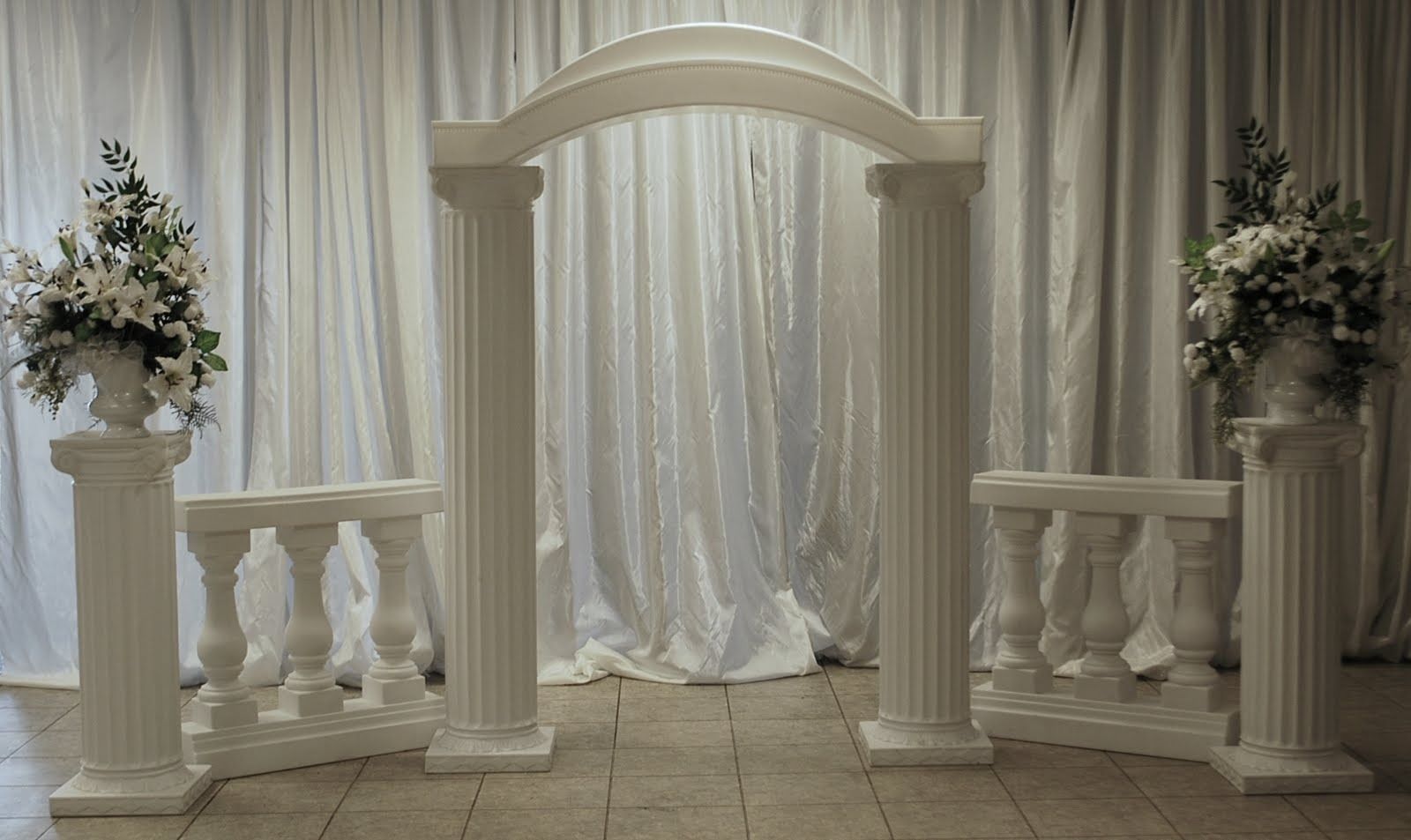 Elegant white wedding arch with draped curtains and floral arrangements on either side