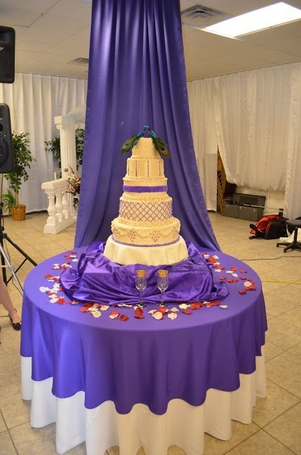 Decorated tiered cake on a purple-draped table at an indoor event hall