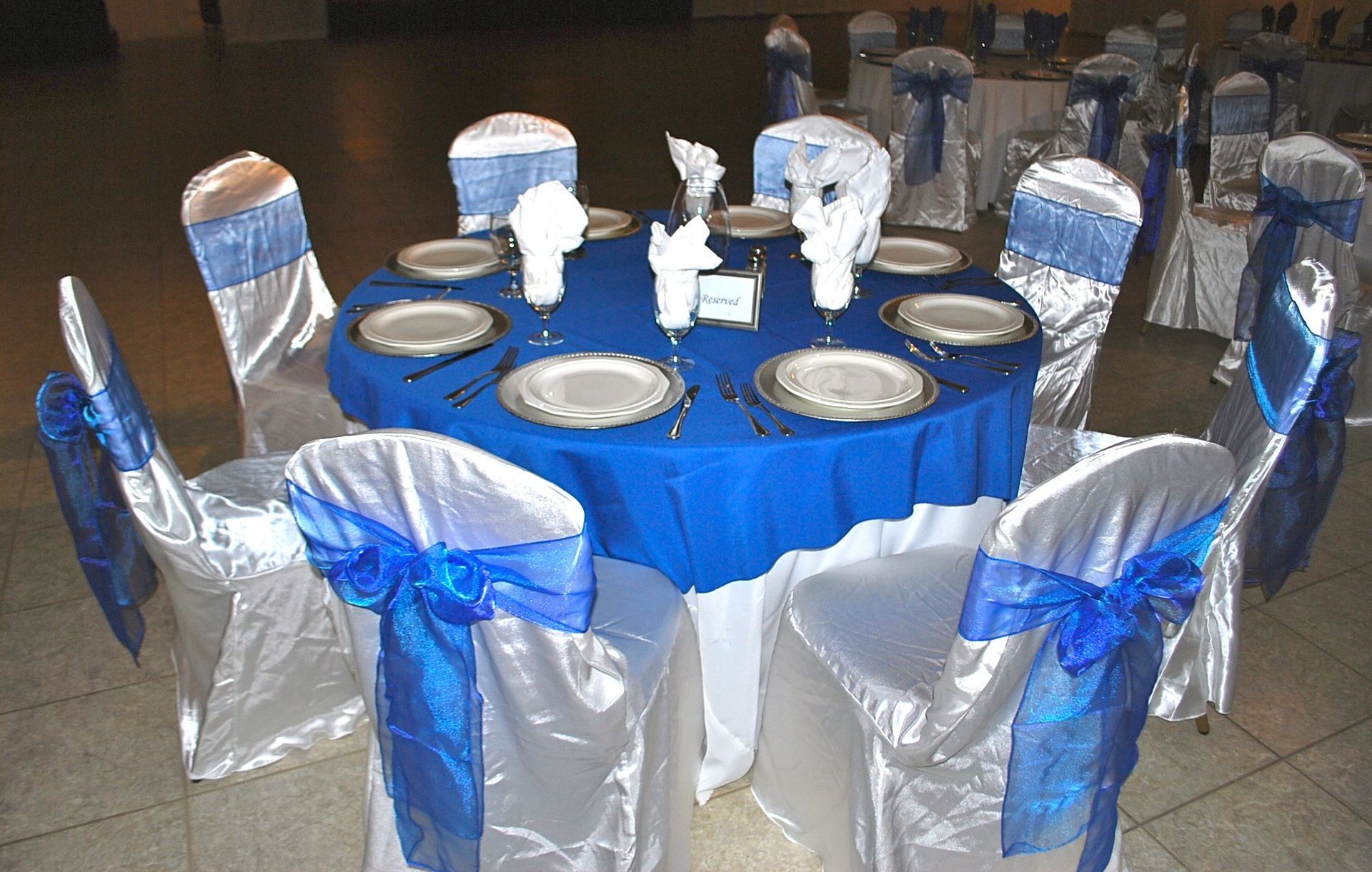 Round banquet table with blue tablecloth and silver chair covers set for an event