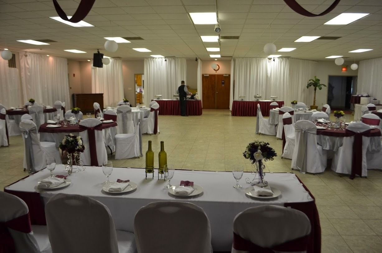 Banquet hall with round, set tables, white curtains, and a podium at the front.