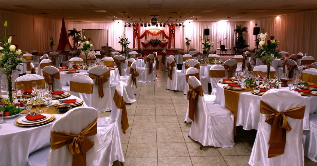 Decorated banquet hall with round tables, white chair covers, and a wedding stage at the far end