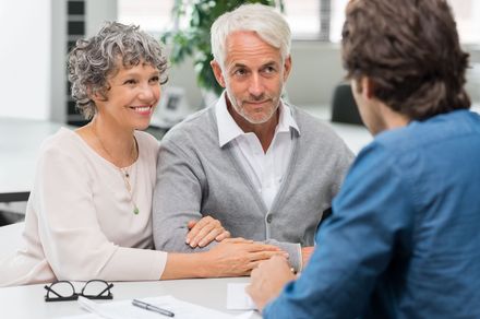Three people in a meeting, with an older couple speaking to a man across the table