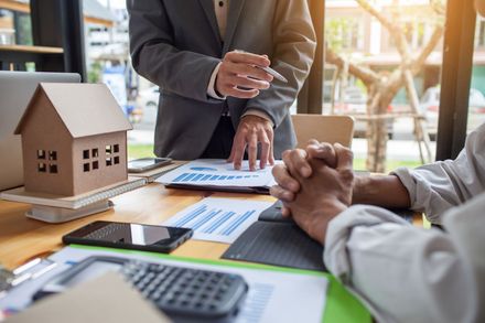 Real estate meeting with a house model, documents, calculator, and hands discussing a contract on a table