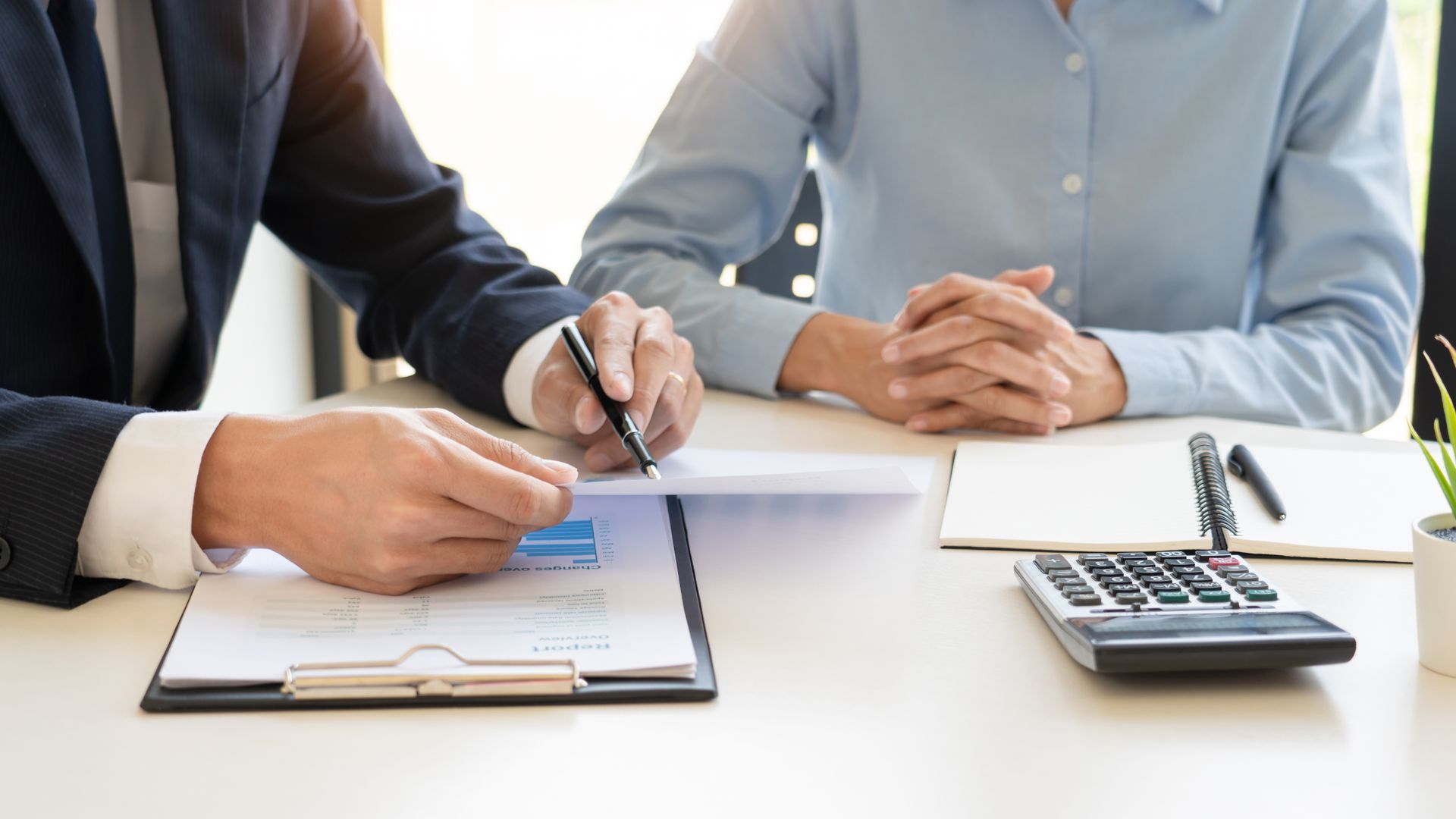 Two people in business attire reviewing documents at a desk with a calculator and clipboard