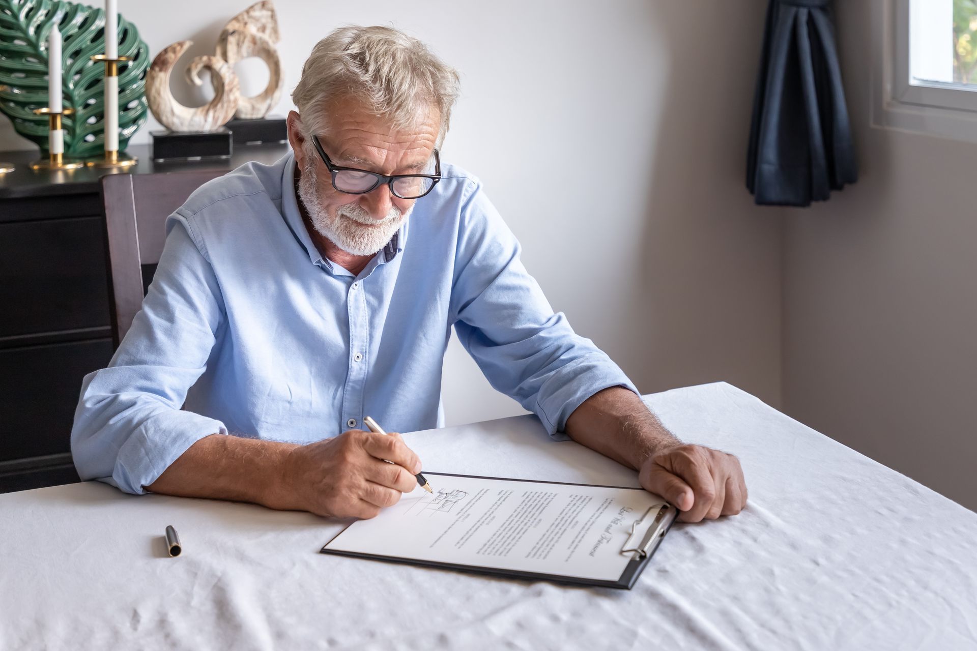 Man signing papers at a table in a bright room with a white tablecloth Man signing papers at a table in a bright room with a white tablecloth