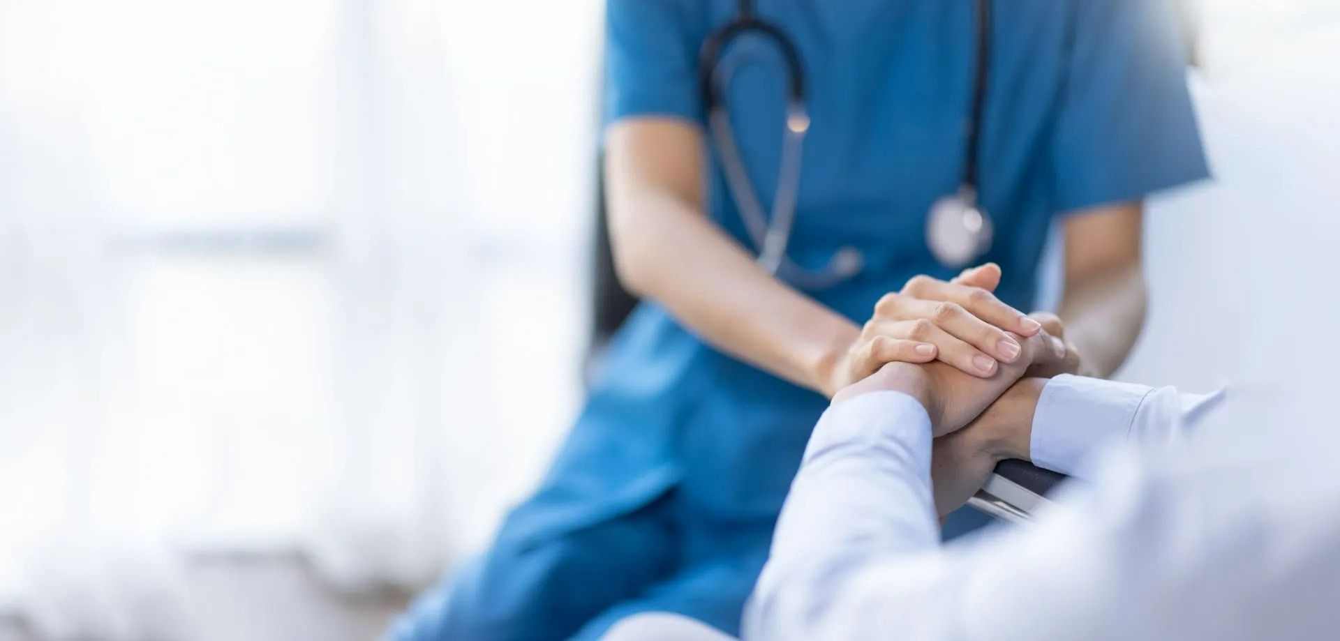 Nurse in blue scrubs holding a patient’s hand in a hospital setting