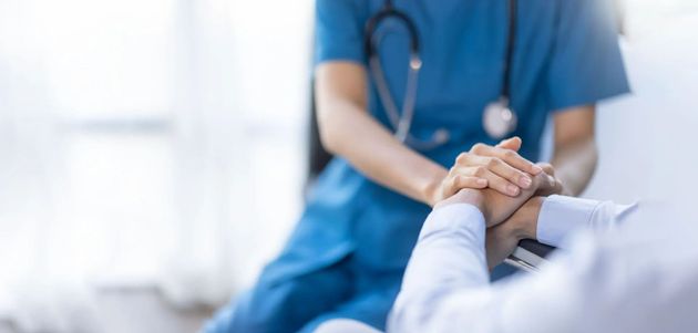 Nurse in blue scrubs holding a patient’s hand in a hospital setting