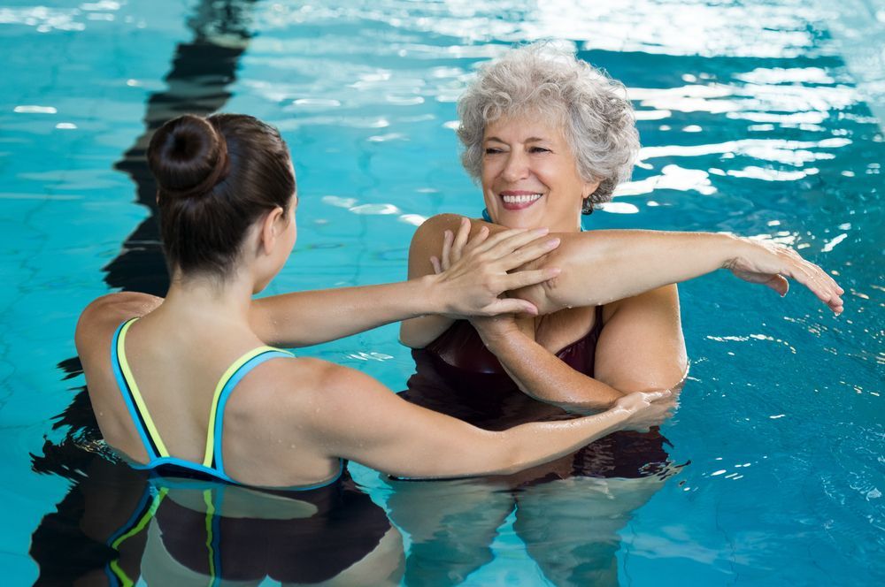 A Woman is Helping an Older Woman Stretch Her Arms in a Swimming Pool — North Wyong Aqua Centre In Wyong, NSW