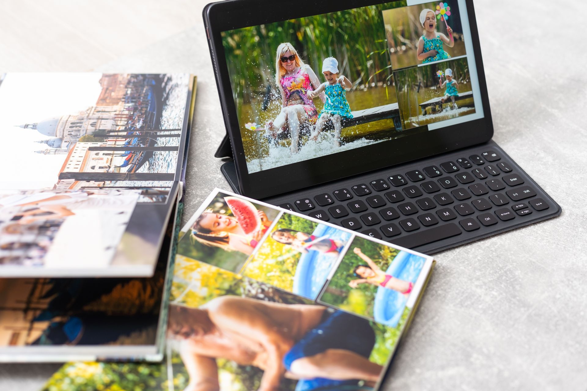 Tablet displaying family photos beside printed photo albums on a light table.