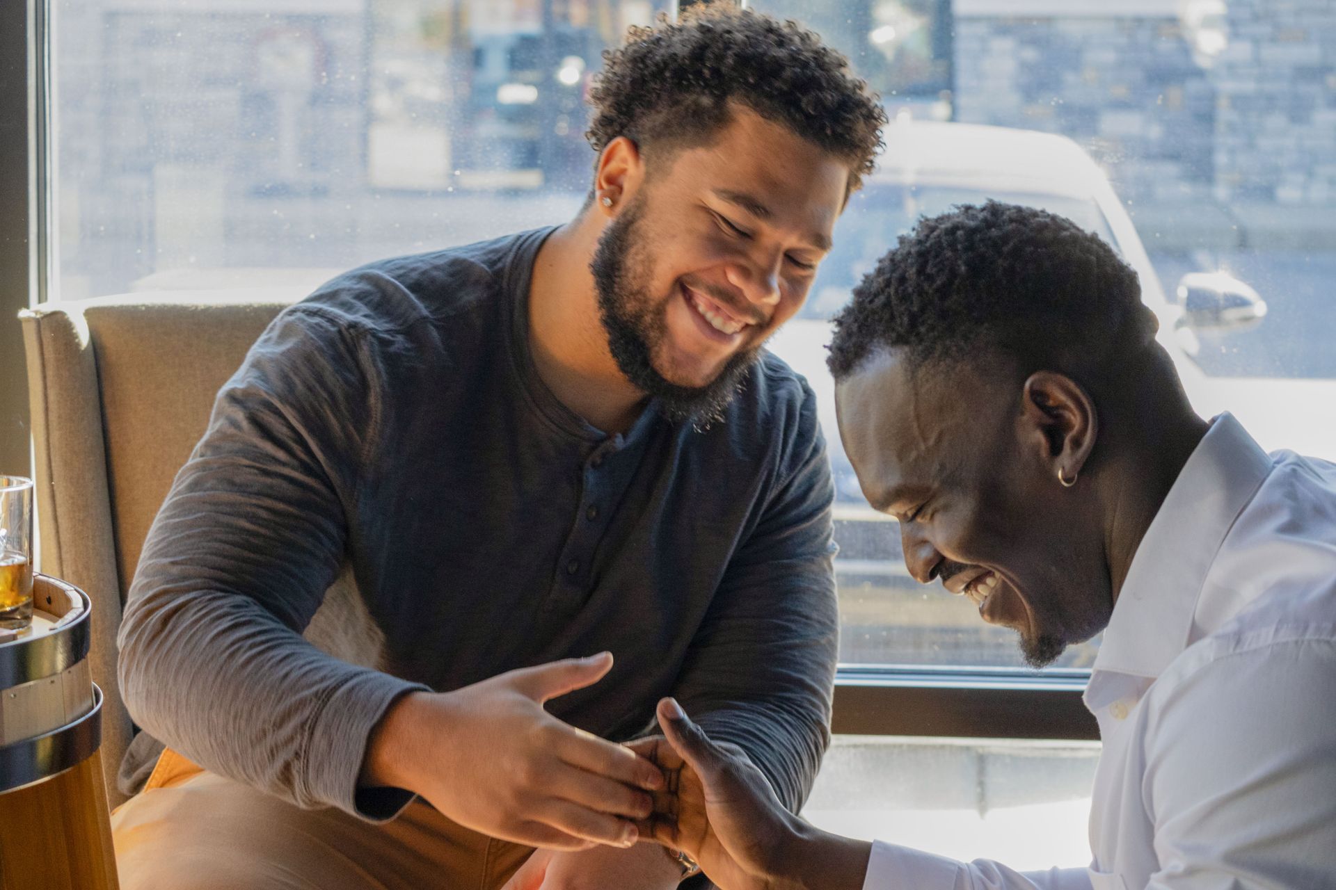 Two men are sitting at a table holding hands and smiling.