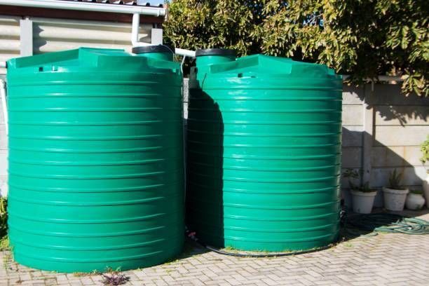 Two green water tanks are sitting next to each other on a brick driveway.