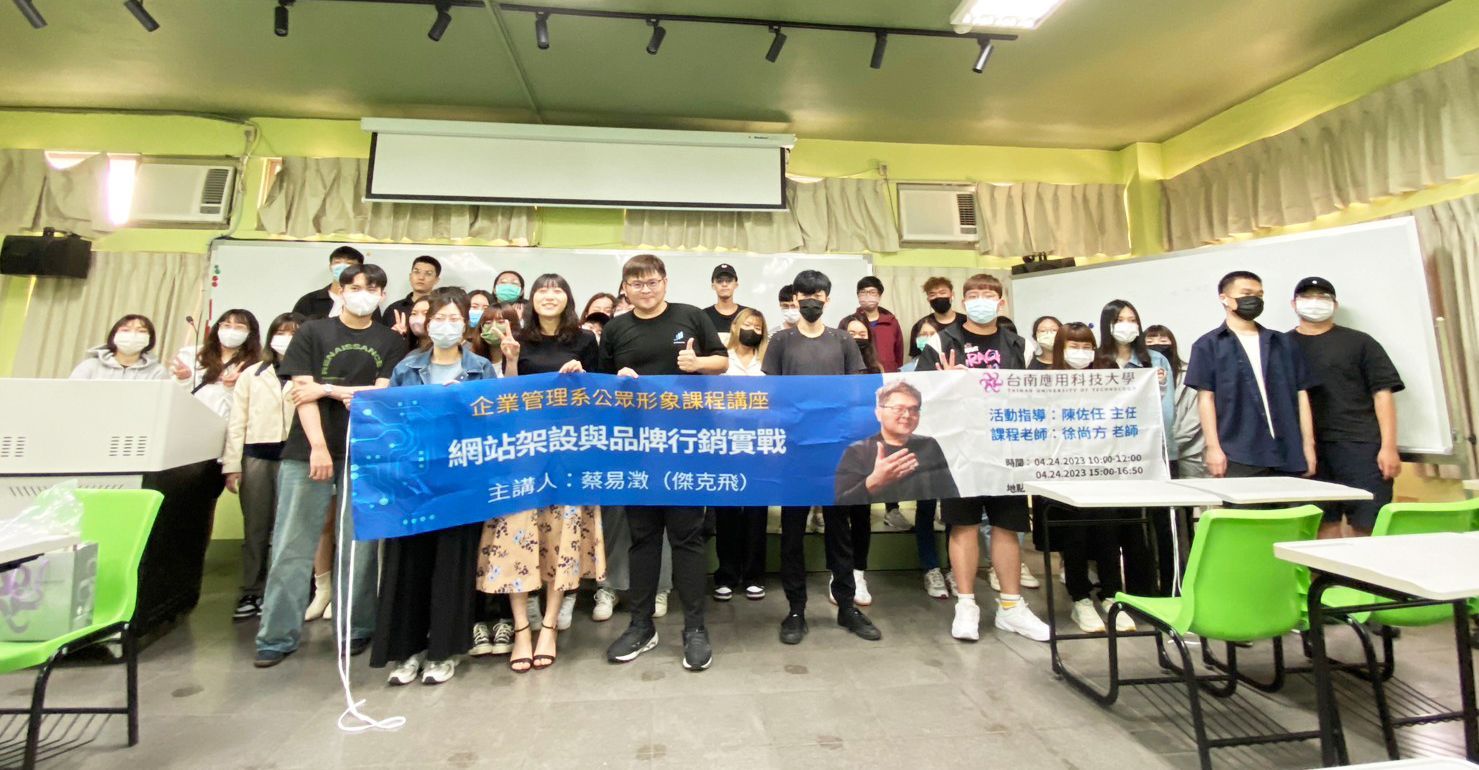 A group of people are standing in a classroom holding a banner.