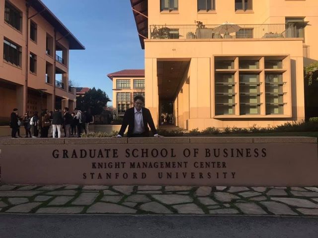 A man sits in front of a sign that says graduate school of business