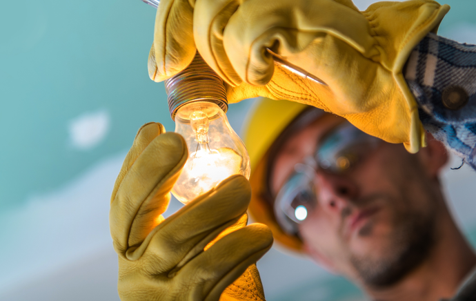 A man in a hard hat and gloves is holding a light bulb.