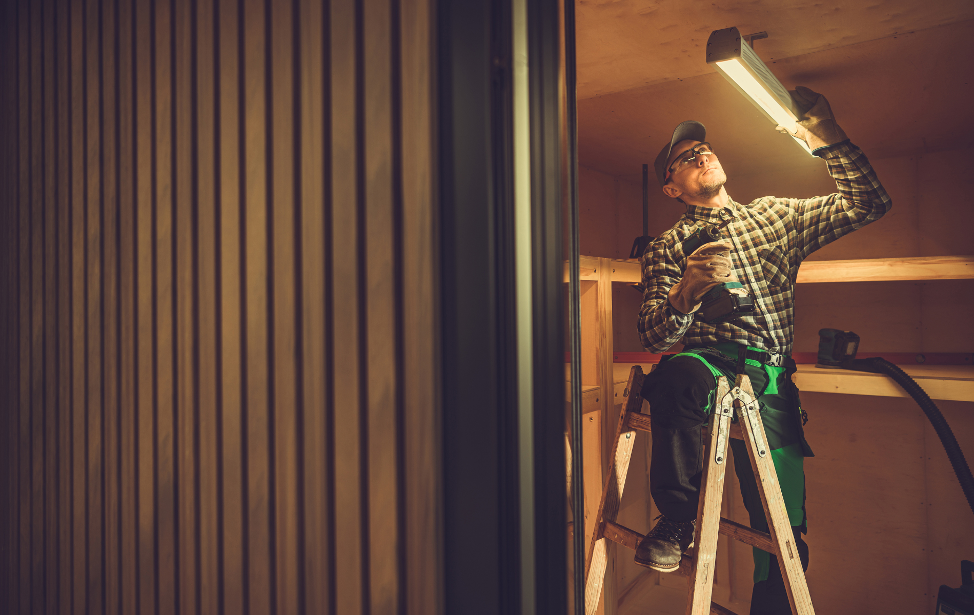 A man is standing on a ladder fixing a light fixture.