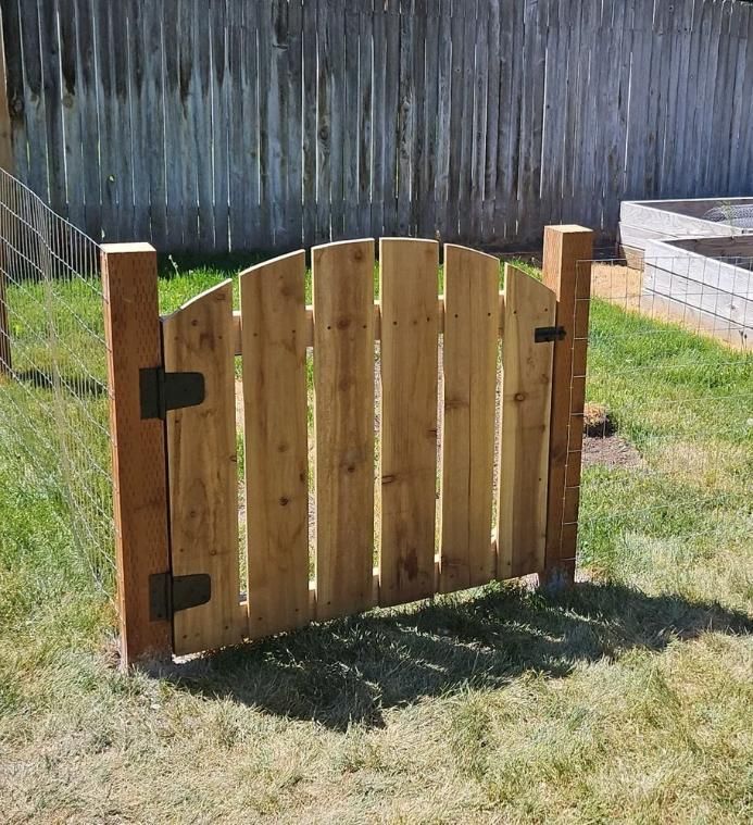 Small wooden garden gate with black hinges in a fenced grassy yard.
