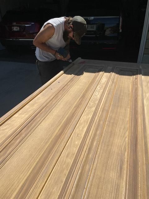 Worker sanding a large wooden board in a garage with a power tool