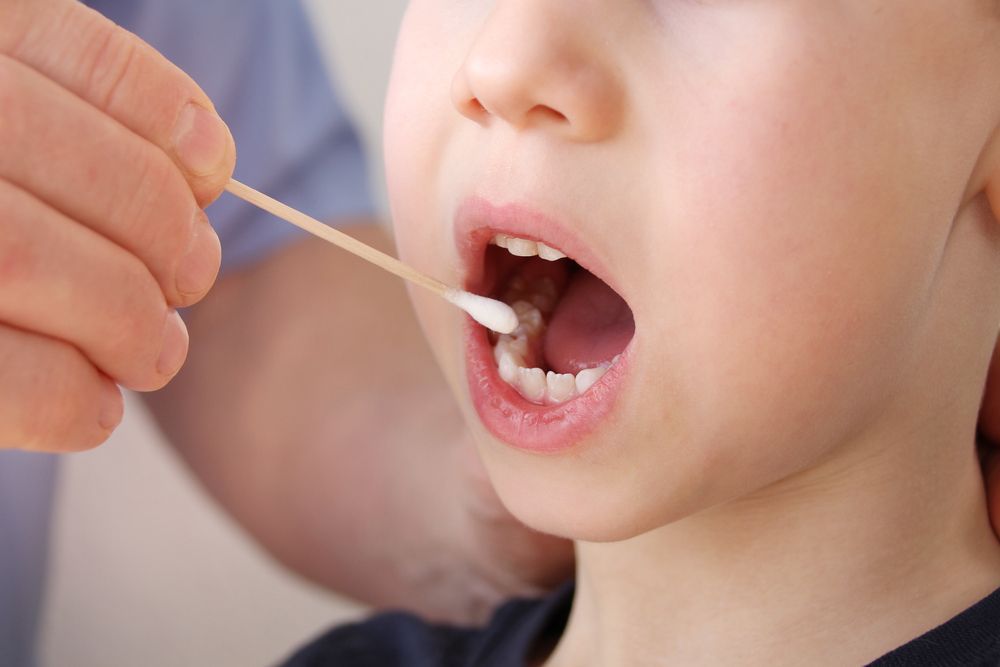 A child is being examined by a doctor with a swab in his mouth.