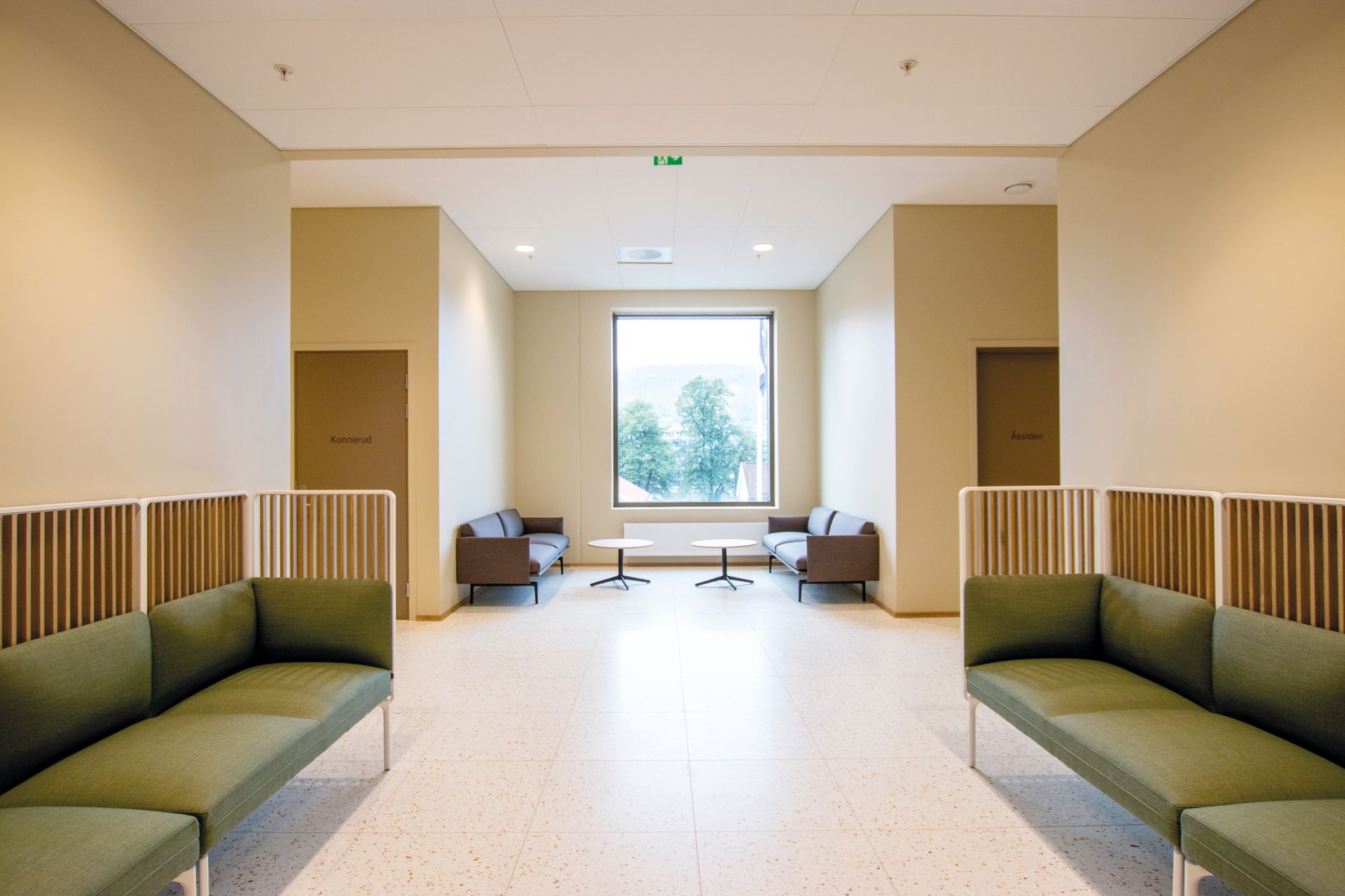 Et venterom med grønne sofaer og et stort vindu.