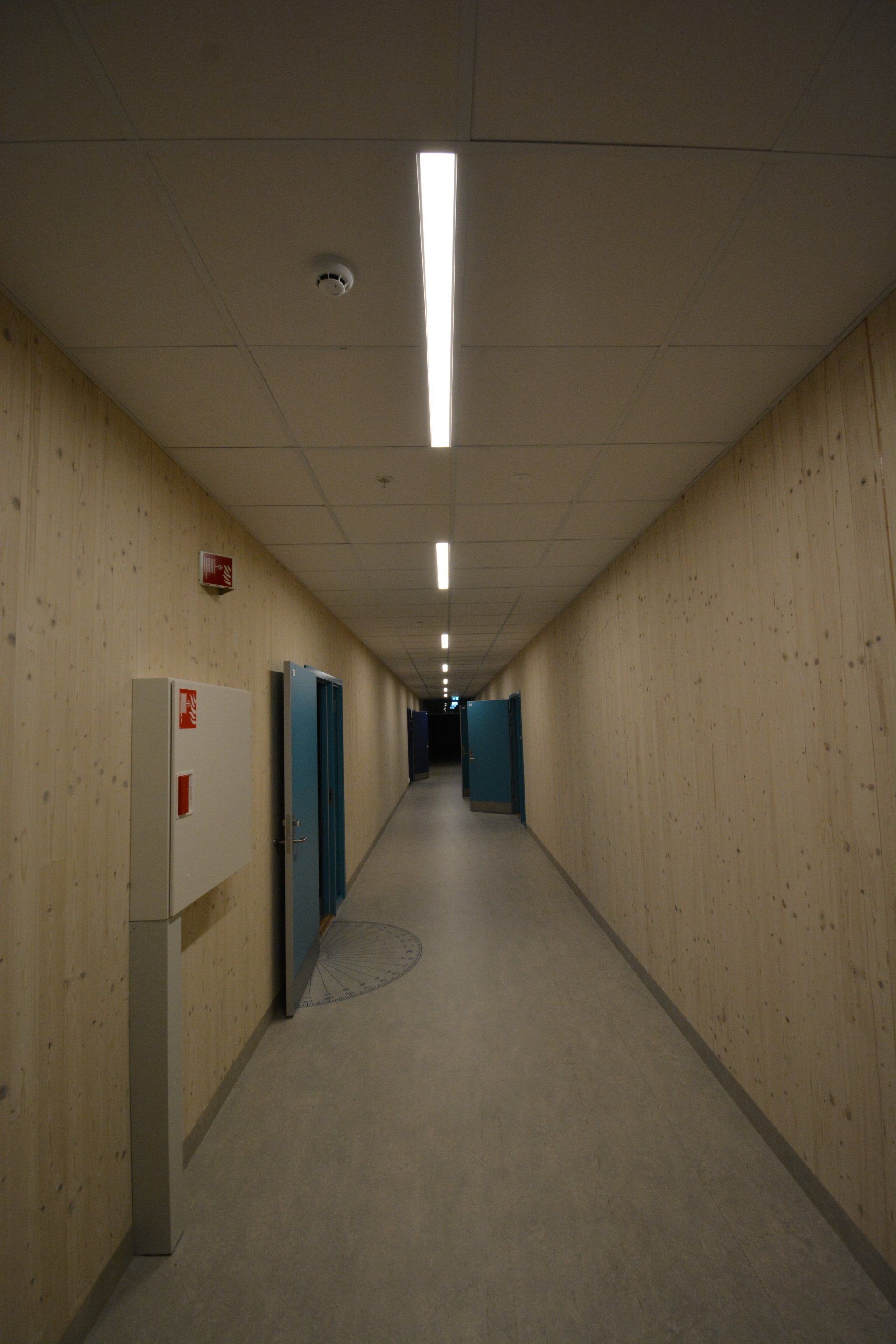 En lang gang med trevegger og lys i taket.