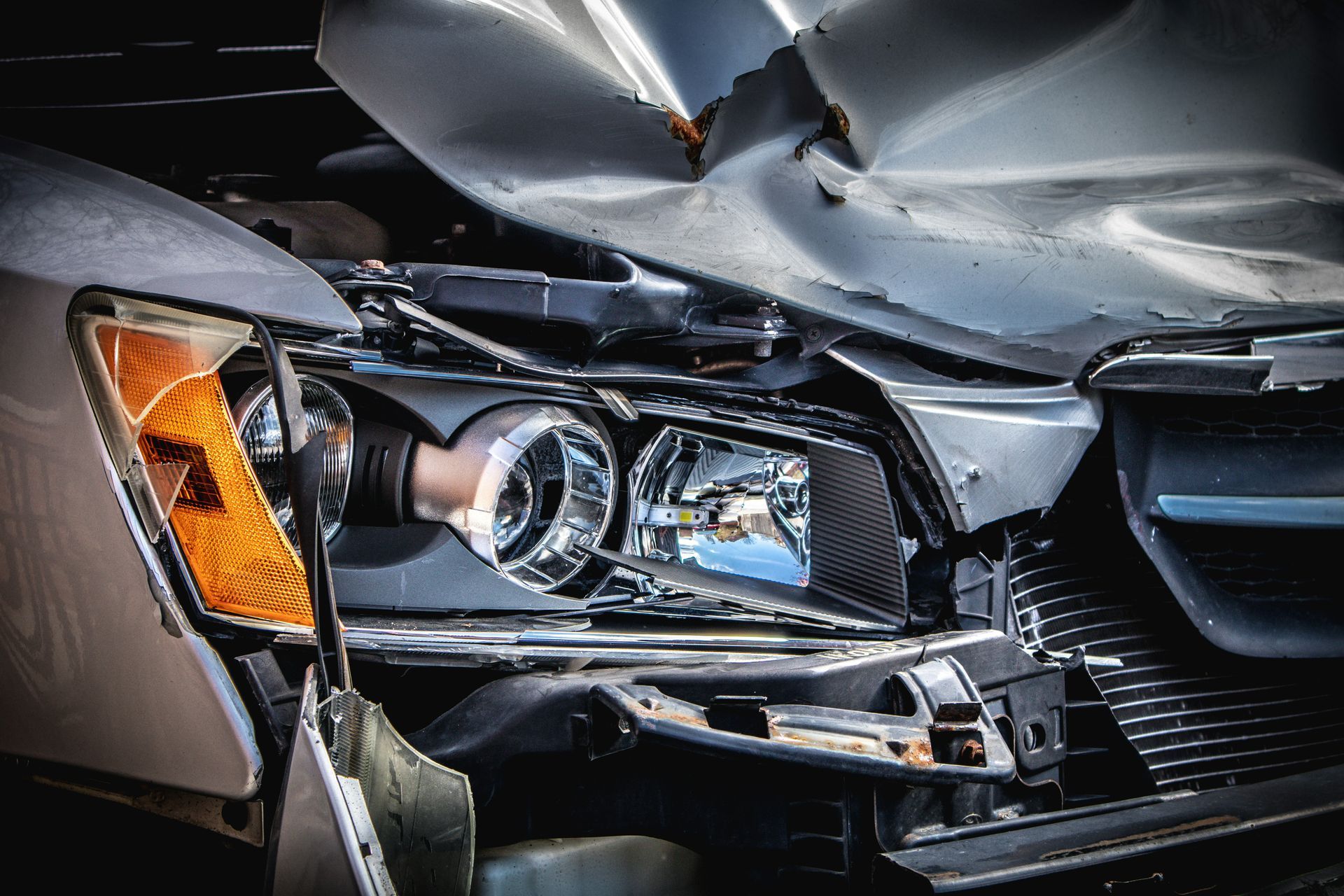 Front view of a black car with a crushed hood and damaged headlight after a collision